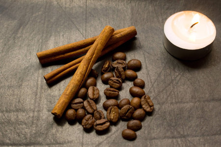 cinnamon sticks, coffee beans, lighted candle on a black backgroundの写真素材