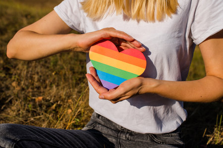 Woman holds in hands a heart in the colors of the rainbow. Young beautiful girl. LGBT history month. Pride Month. Lesbian Gay Bisexual Transgender. LGBT flag. Love and toleranceの写真素材