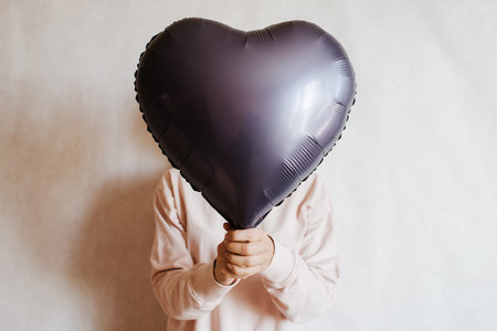 The girl holds a heart-shaped air balloon in her hands. Caucasian woman enjoy party. Happy...