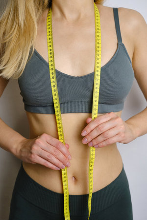 A body centimeter in the hands of girl in tracksuit after a workout or fitness session. Measurement of body volume. Sports waist. Healthy lifestyle, physical activityの写真素材