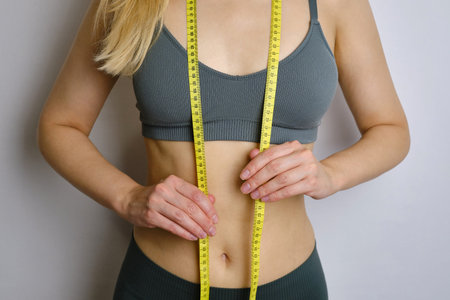 A body centimeter in the hands of girl in tracksuit after a workout or fitness session. Measurement...