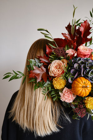Rich bouquet with autumn flowers and a pumpkin in the hands of a girl on a light background. Bright festive bouquet. A holiday gift. Beautiful autumn flowers. Florist girlの写真素材