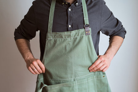 A man in a kitchen apron. Chef work in the cuisine. Cook in uniform, protection apparel. Job in food service. Professional culinary. Green fabric apron, casual stylish clothingの写真素材
