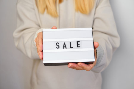 Light box with text SALE in the hands of a girl. Season sale, holiday shopping. Special offer for...