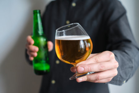A glass of beer and bottle in the hands of a man. Tasting brewed craft beer. Lager beer with beautiful foam. Cold refreshment beverage. Alcohol drink. Relaxation and enjoymentの写真素材
