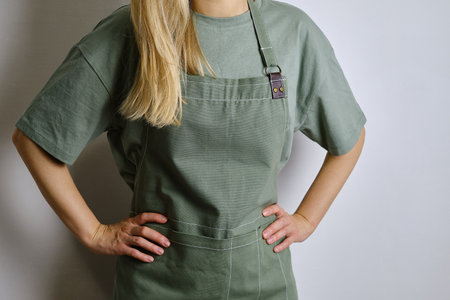 A woman in a kitchen apron. Chef work in the cuisine. Cook in uniform, protection apparel. Job in food service. Professional culinary. Green fabric apron, casual clothingの写真素材