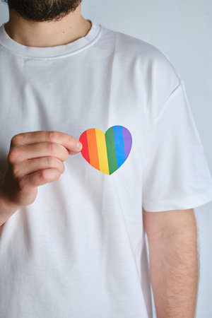 Rainbow heart from paper in man hands in white t-shirt. LGBT flag. LGBTQIA Pride Month in June....