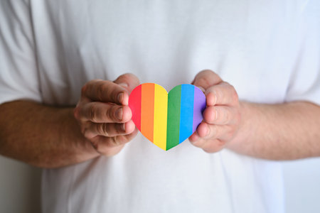 Rainbow heart from paper in man hands in white t-shirt. LGBT flag. LGBTQIA Pride Month in June. Lesbian Gay Bisexual Transgender. Gender equality and tolerance. Rainbow flagの写真素材