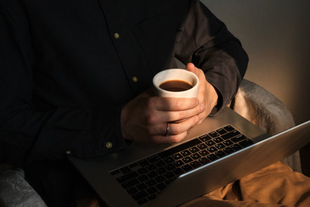 Businessman holding in hands laptop and cup of delicious coffee. Man drinking morning hot espresso and making job from home. Online remote work. Modern freelancer lifestyleの写真素材
