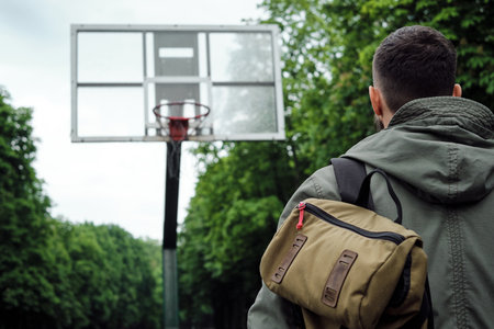 A man standing in front of a basketball basket. Focused on the goal, looking at the basketball basket. Street basketball. Walk in the park with a backpack on a rainy dayの写真素材