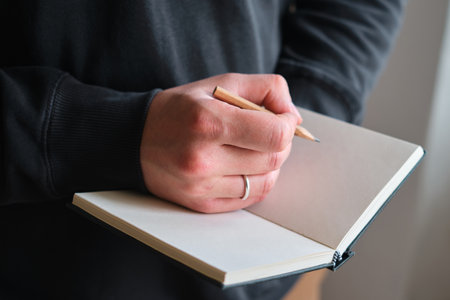 A man makes sketches or notes with a pencil. Writing or drawing on blank paper in notebook. Artist create artwork in sketchbook. Planning a new creative idea. Work on projectの写真素材