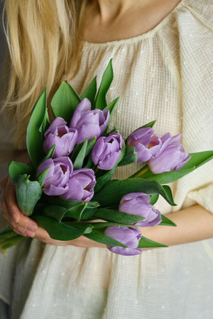 Happy woman holds purple tulips in her hands. Florist girl gathered a bouquet. Beautiful lavender flowers. Blossom petal. Gift for the holiday celebration, springtime moodの写真素材