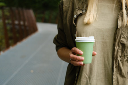 Green paper cup with coffee in woman hand. Time for drink coffee in city. Coffee to go. Enjoy moment, take a break. Disposable paper cup closeup. Delicious hot beverageの写真素材
