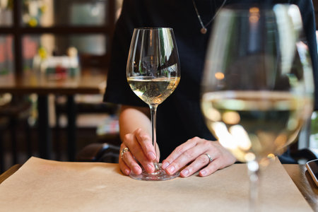 A glass of white wine in the hands of a girl relaxing in a restaurant. Tasting of alcoholic...
