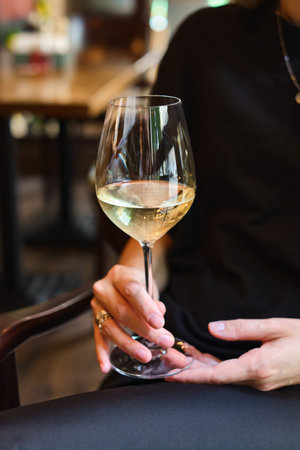 A glass of white wine in the hands of a girl relaxing in a restaurant. Tasting of alcoholic beverages. Summer rest. Romantic evening aperitif. Close-up of a glass of wineの写真素材