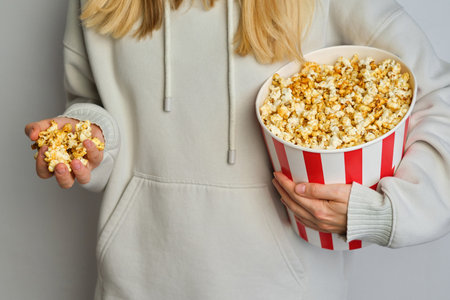 Popcorn paper bucket in the hands of a young girl preparing to watch a movie. Showtime. Eating delicious unhealthy sweet snacks. Going to cinema for a new filmの写真素材