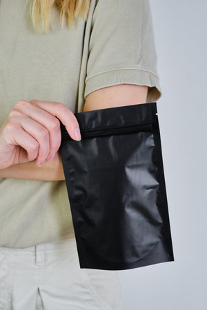 Kraft black paper packaging in a woman hands. Packaging for coffee, cosmetics. Packing closeup....