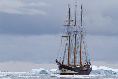 small sailing ship in Antarctic waters between ice floes and icebergs