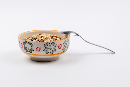 Bowl full of oatmeal with a spoon of stainless steel on a white backgroundの写真素材