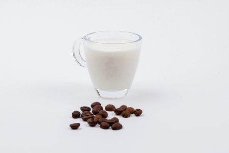 A glass mug full of milk next to coffee beans on a white stench. Isolatedの写真素材