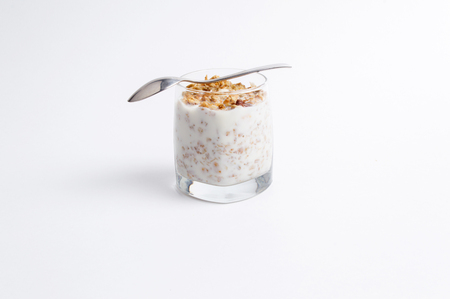 Glass full of muesli and milk with stainless steel spoon on a white backgroundの写真素材