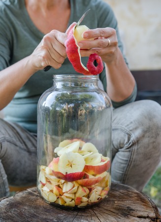 Woman makes apple vinegar - peeling apple and cut it into a bottleの写真素材