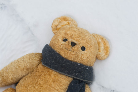 Teddy bear in scarf lay on the snow and making snow angel - European scene with an old toy