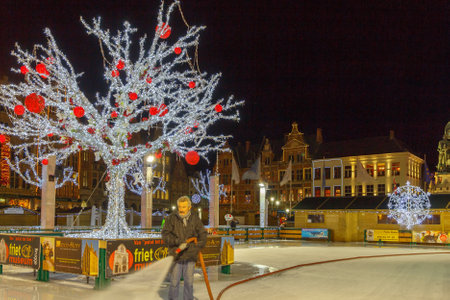 Bruges, Belgium - December 24, 2014: Central Bruges Market Square decorated at Christmas. A man pours water at night skating rink.のeditorial素材