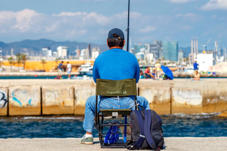 Barcelona, Spain - September 5, 2015: Barceloneta is one of the most popular city beaches of Barcelona. Many tourists come here to sunbathe, swim and play sports. Fishermen catch fish from piers.のeditorial素材