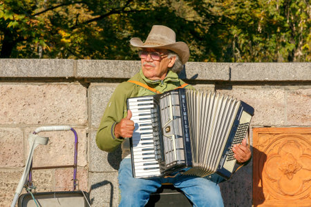 Riga, Latvia - 15 October, 2015: Old man in a hat entertains tourists playing the accordion at the Independence Square in Riga. Street musicians One of the attractions of the Latvian capital.のeditorial素材