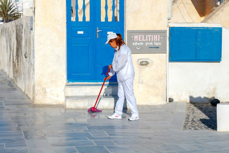 Oia, Greece - April 27, 2016: A cleaning lady washes the street in the village Oia in the early morning on the island Santarini. Village daily visited by many tourists.のeditorial素材
