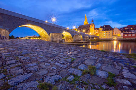 Regensburg. Old stone bridge over the Danube river at night light.の写真素材