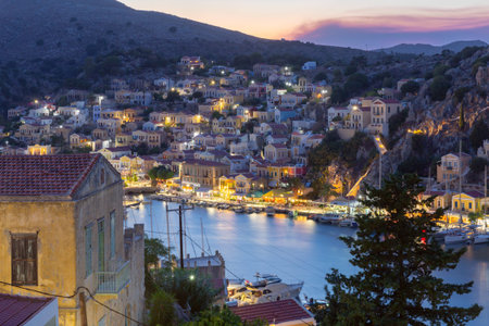 Multi-colored facades of houses in the light of lanterns in the village of Symi at sunset.