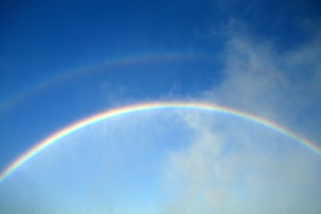 Primary and secondary rainsbows against a deep blue sky.の写真素材