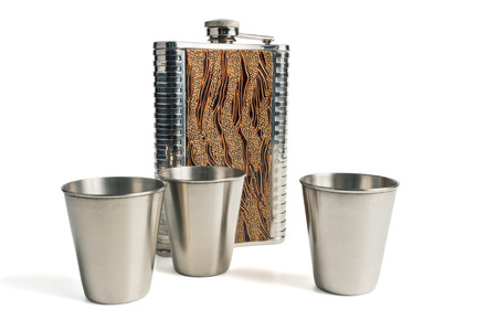 Metal flask trimmed leather and three metallic, sturdy shot glasses on a white backgroundの写真素材
