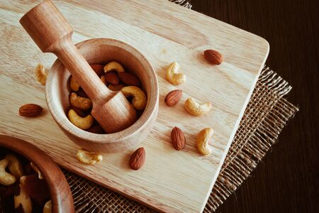 A mixture of various nuts in a wooden mortar and pestle made of hard wood on a cutting boardの写真素材