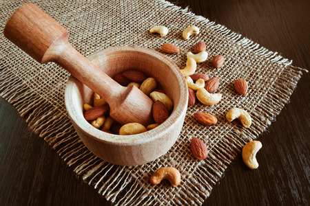 A mixture of various nuts in a wooden mortar and pestle made of hard wood on a napkin of coarse clothの写真素材