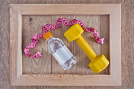 Dumbbells, measuring tape and a bottle of water in a frame on a wooden backgroundの写真素材