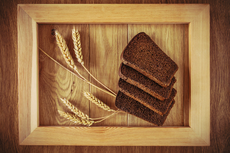 Sliced rye bread and spikelets of rye in a wooden frame, on a wooden surfaceの写真素材