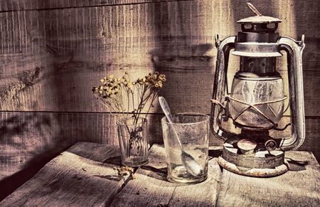 An old, dusty kerosene lamp called a "bat" in the corner of an old table on the background of a wooden wallの写真素材