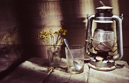 An old, dusty kerosene lamp called a "bat" in the corner of an old table on the background of a wooden wallの写真素材