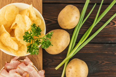 Still life with chips and raw potatoes, bacon and green onions on a dark wooden backgroundの写真素材