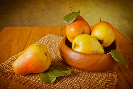 Ripe pears on a wooden table and in a wooden bowl with green leavesの写真素材