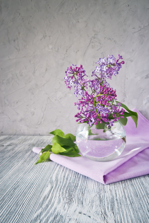 Sprig of lilac in a glass round vase on a wooden table still lifeの写真素材