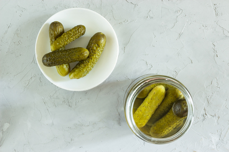 Gherkins marinated in a glass jar and in a bowl on a gray concrete backgroundの写真素材