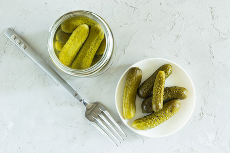 Gherkins marinated in a glass jar and in a bowl on a gray concrete backgroundの写真素材