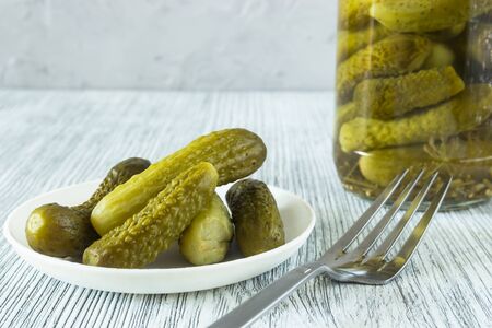 Pickled gherkins in a glass jar and in a bowl on a gray wooden backgroundの写真素材