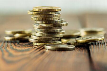 Uneven stack of dark yellow coins with scattered coins on a wooden background, close-upの写真素材