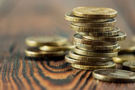 Uneven stack of dark yellow coins with scattered coins on a wooden background, close-upの写真素材