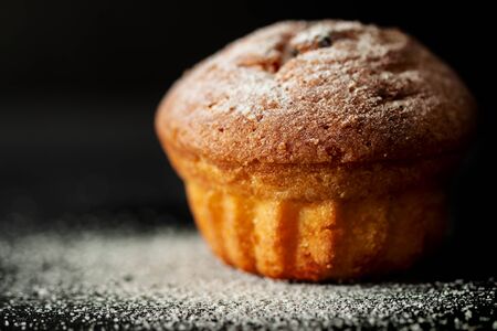 Baked muffin with sugar powder close-up on a black backgroundの写真素材